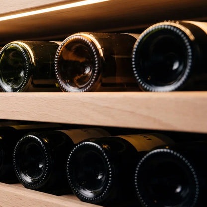 Wine bottles resting on solid beech shelves under the warm interior lighting of a Maison Vinum wine cellar